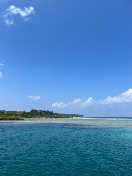 Free Peaceful tropical landscape with clear turquoise waters and lush island under a bright blue sky. Stock Photo