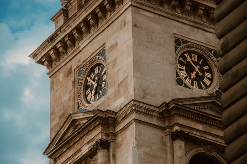 Free Low angle shot of a historic clock tower with Roman numerals, showcasing architectural details against a cloudy sky. Stock Photo