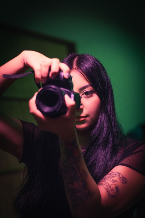 Free Creative studio portrait of a young woman holding a camera, showcasing tattoos and focus. Stock Photo