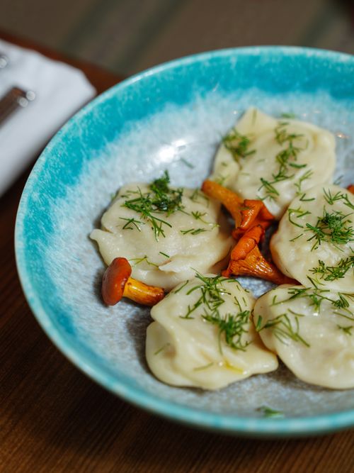 Free Close-up of dumplings garnished with dill and chanterelle mushrooms on a ceramic plate. Stock Photo