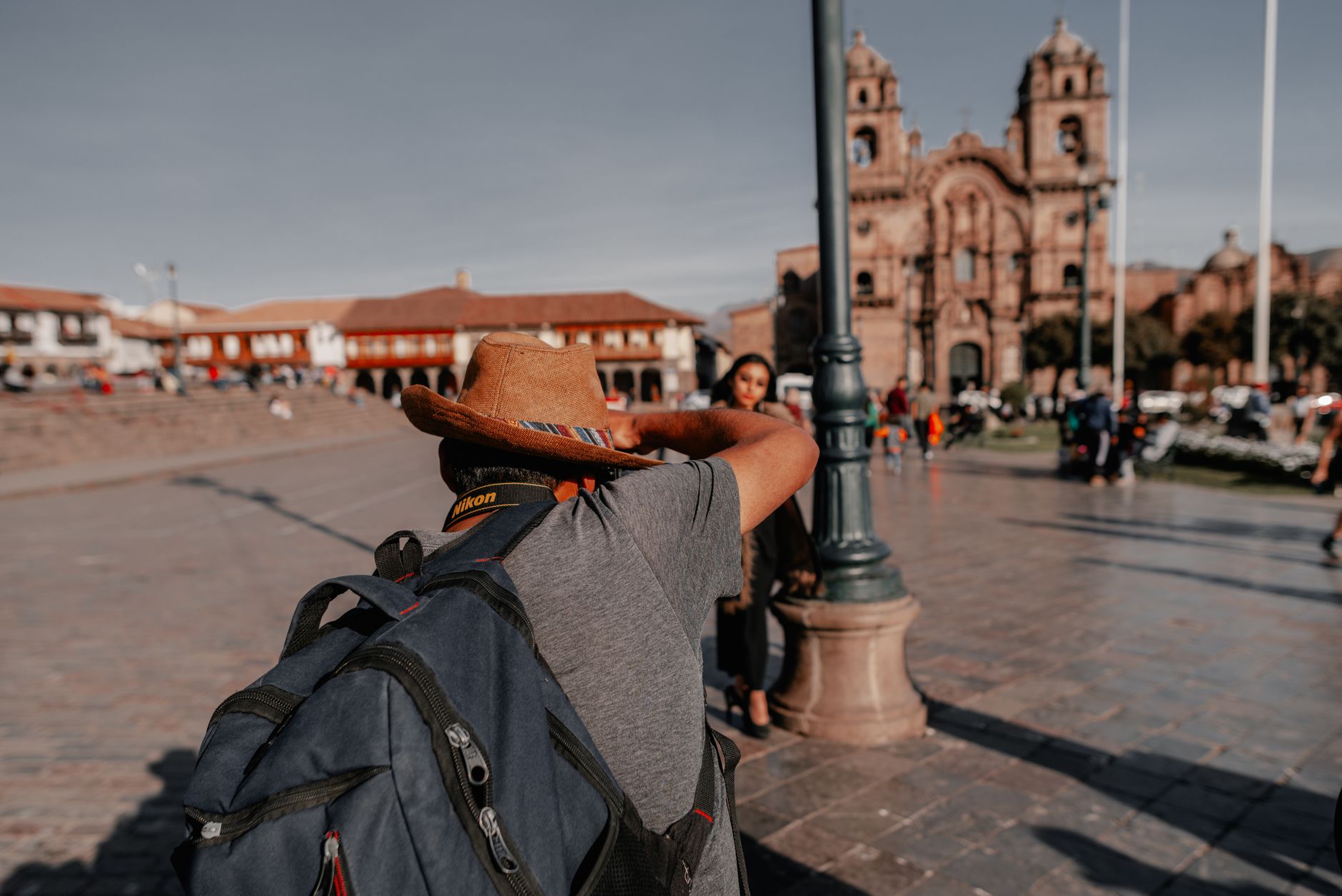 Adult backpacker photographing in a vibrant urban square with historic architecture.