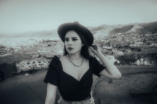 Black and white portrait of a fashionable woman standing outdoors with cityscape background. Urban fashion and style.
