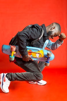 Stylish young man posing with a skateboard against a vibrant red background.