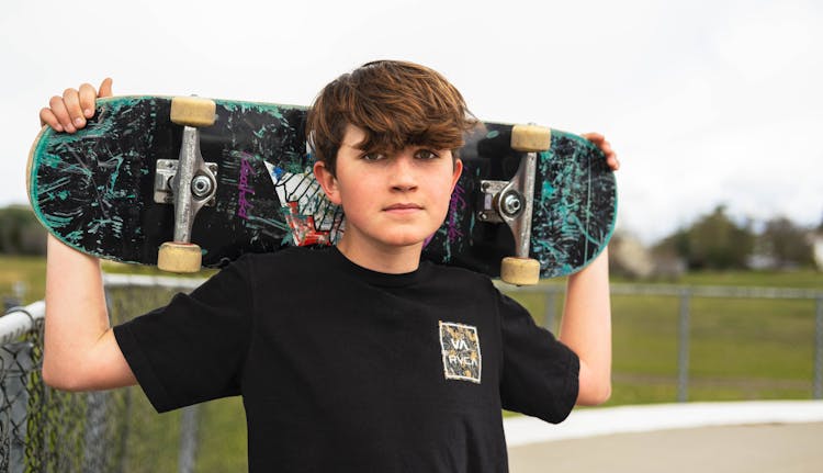 A Boy With A Skateboard Standing Outside 