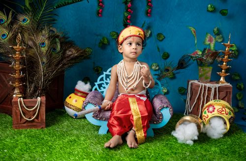 Free A young child in traditional Indian clothing, adorned with jewelry, seated indoors with a colorful background. Stock Photo