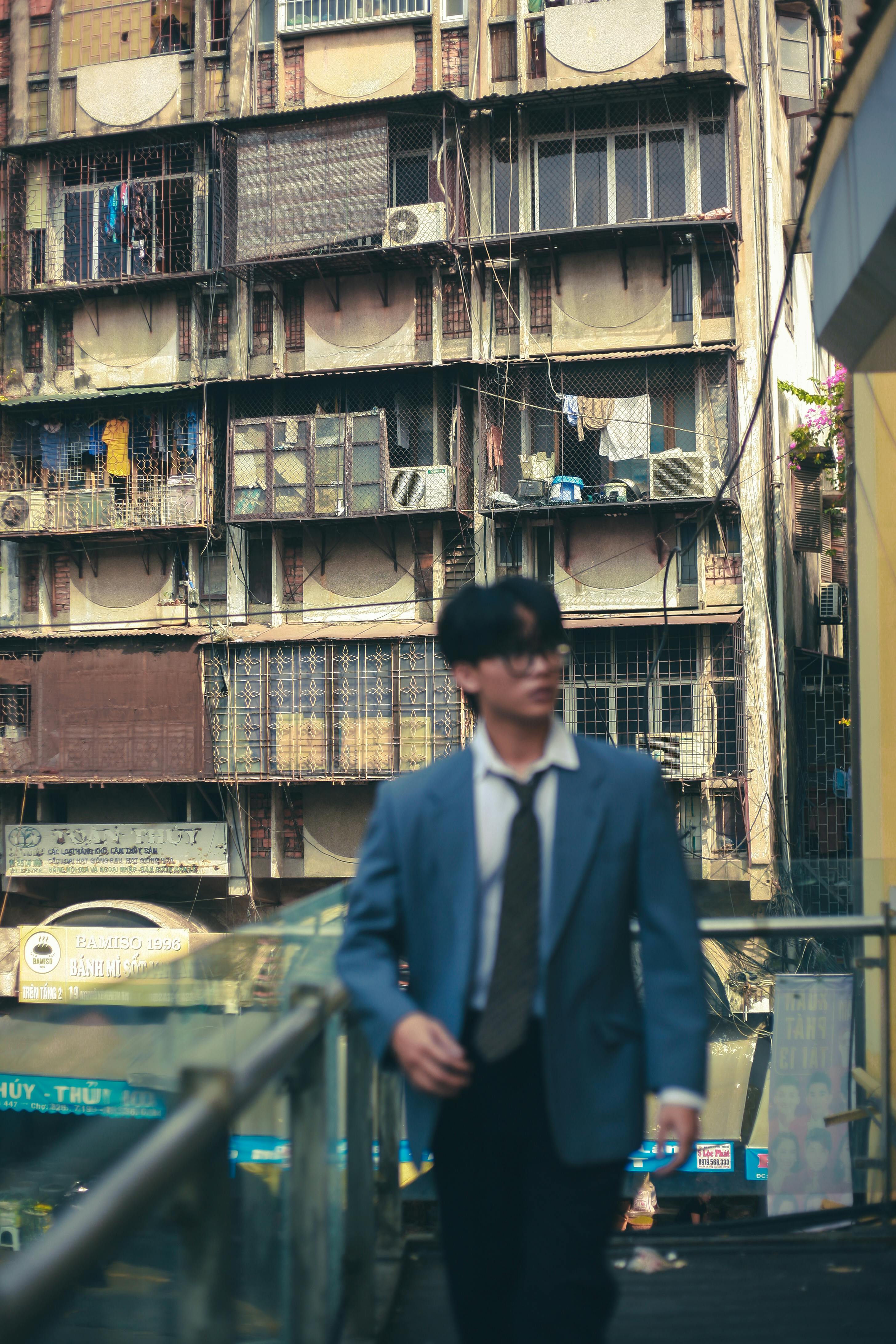 A man in a blue jacket walking past urban residential buildings, showcasing city life.