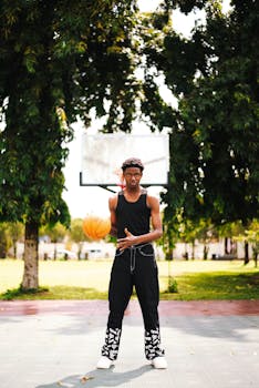 A young man dribbles a basketball on an outdoor court surrounded by trees.
