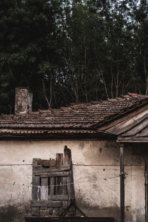 Free A weathered house with broken windows and an old roof set against a rural backdrop. Stock Photo