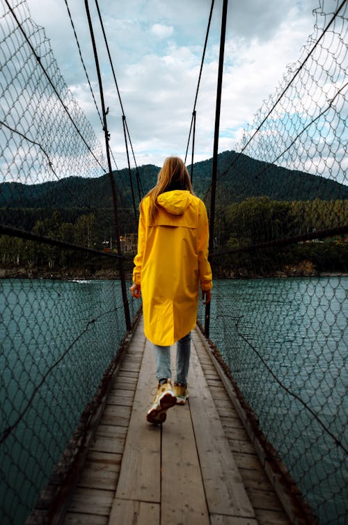 Woman in Yellow Raincoat Walking on Fenced Footbridge