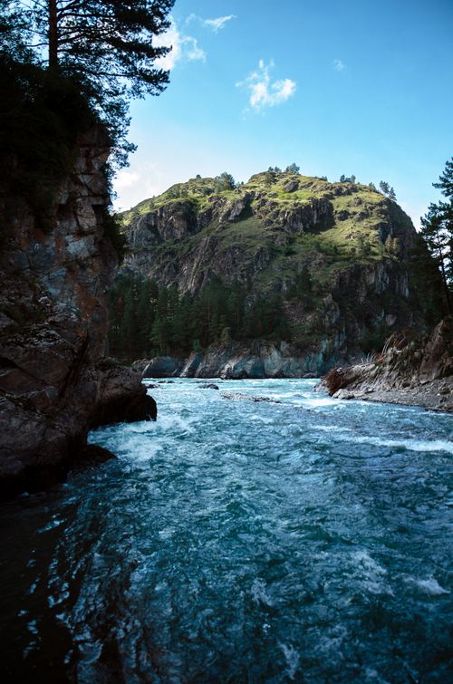 Free Turquoise river rushing through rocky landscape under a bright blue sky with lush green mountain. Stock Photo