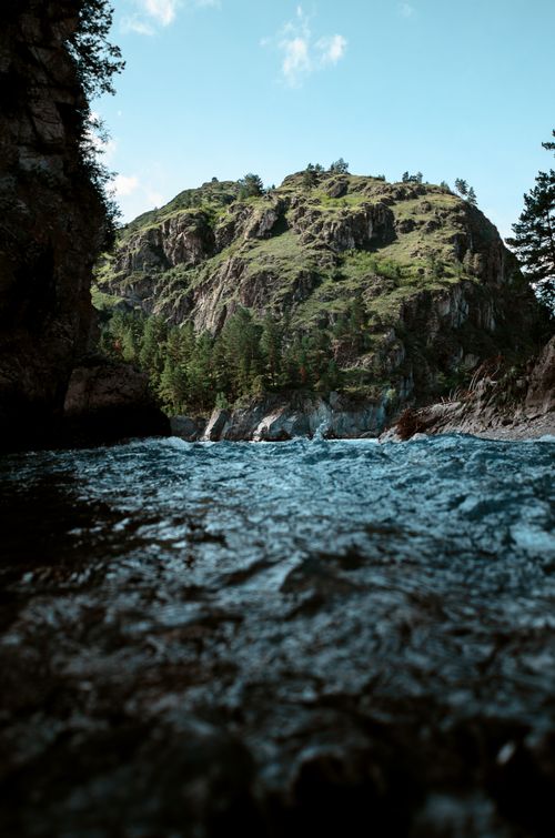 Free A breathtaking view of a flowing river amid mountains and lush greenery under a clear sky. Stock Photo
