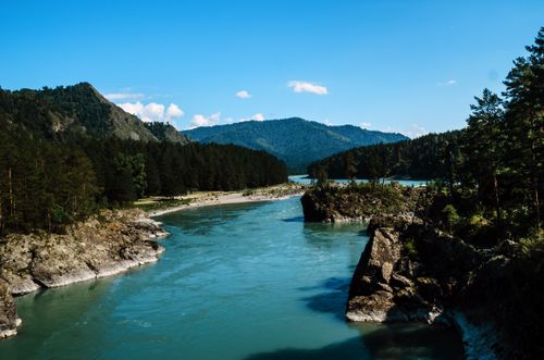 Free A tranquil mountain river scene with lush trees and a clear blue sky, showcasing natural beauty. Stock Photo