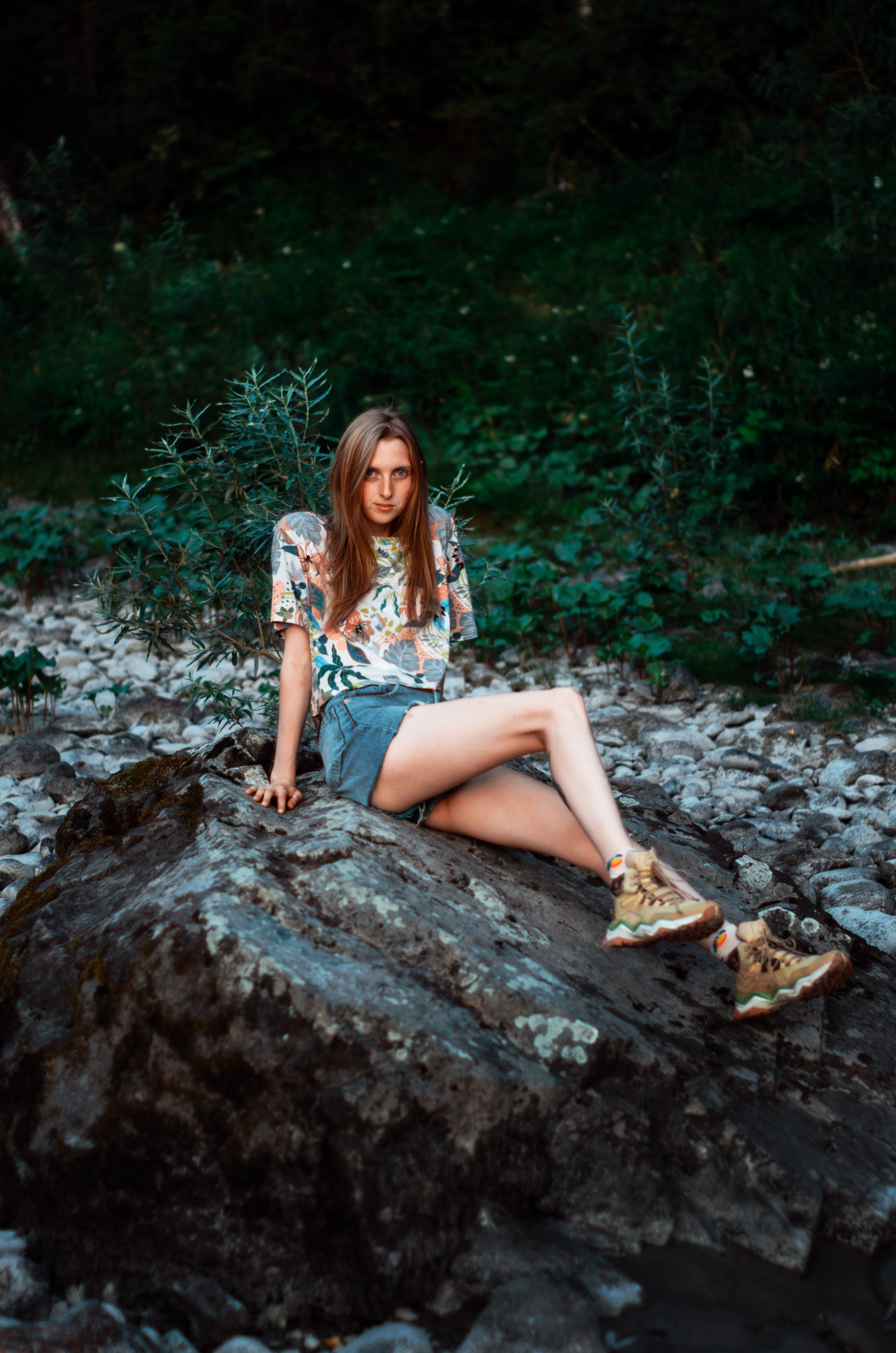 Woman sitting on boulder in nature, wearing casual summer clothing.