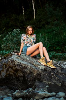 A young woman in hiking attire sitting on a rock in a natural setting.