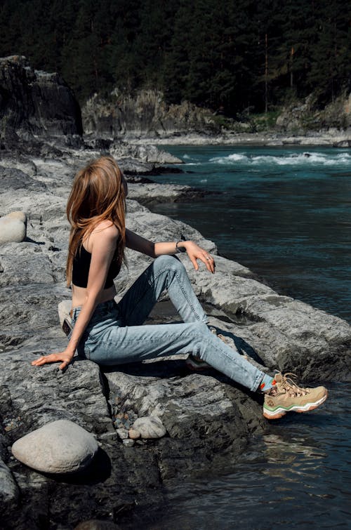 Woman Sitting on a Rock by the Body of Water in Mountains 