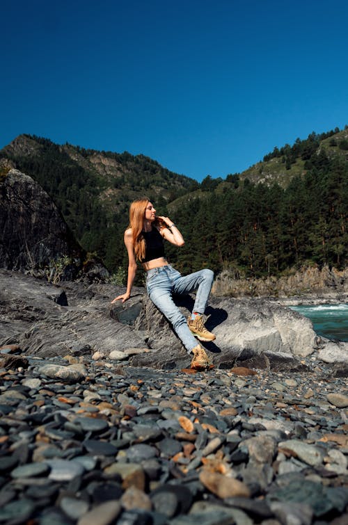 Woman Sitting on a Rock by the Body of Water in Mountains 