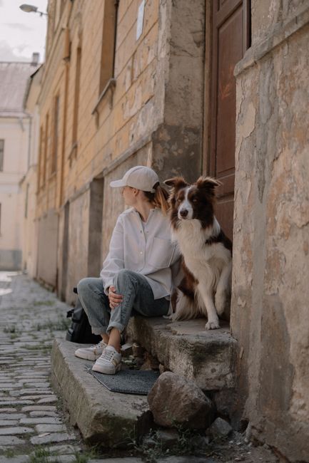A woman and her dog sitting on stone steps in an urban area of Riga, Latvia, enjoying a sunny day.