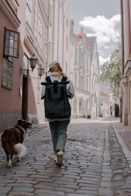 A young woman with a backpack walks her dog through a cobblestone alley in Riga, Latvia.