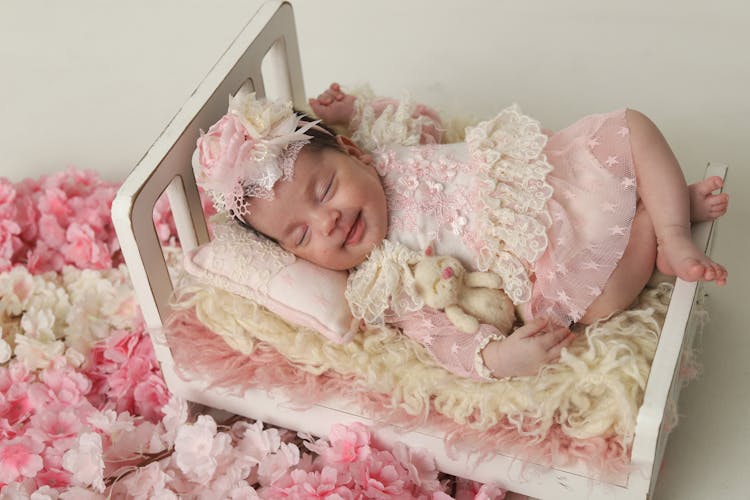 Baby Girl In Dress Sleeping In Bed With Flowers Around