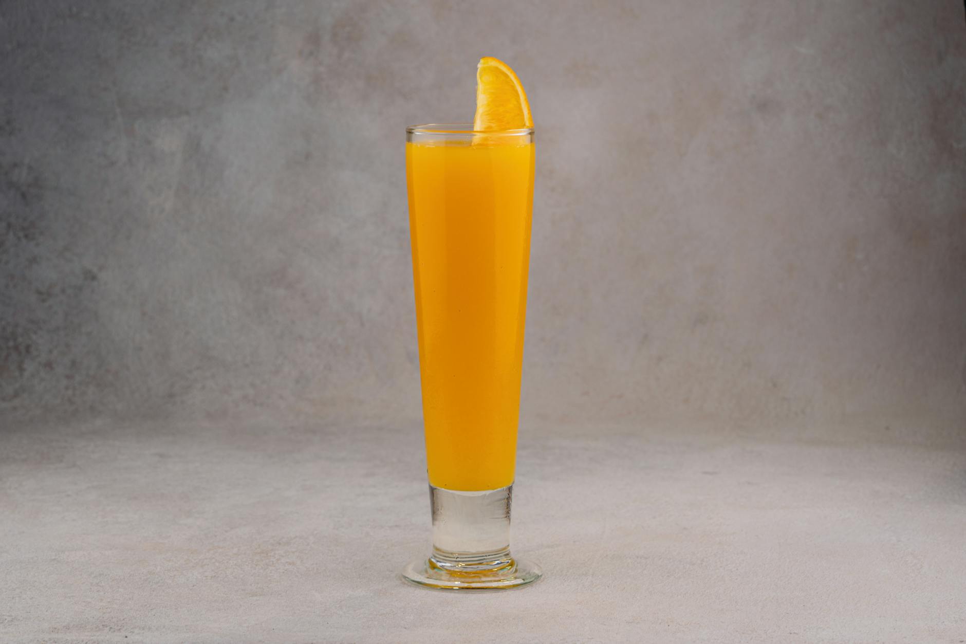 A refreshing glass of orange juice with a slice garnish on a neutral background.