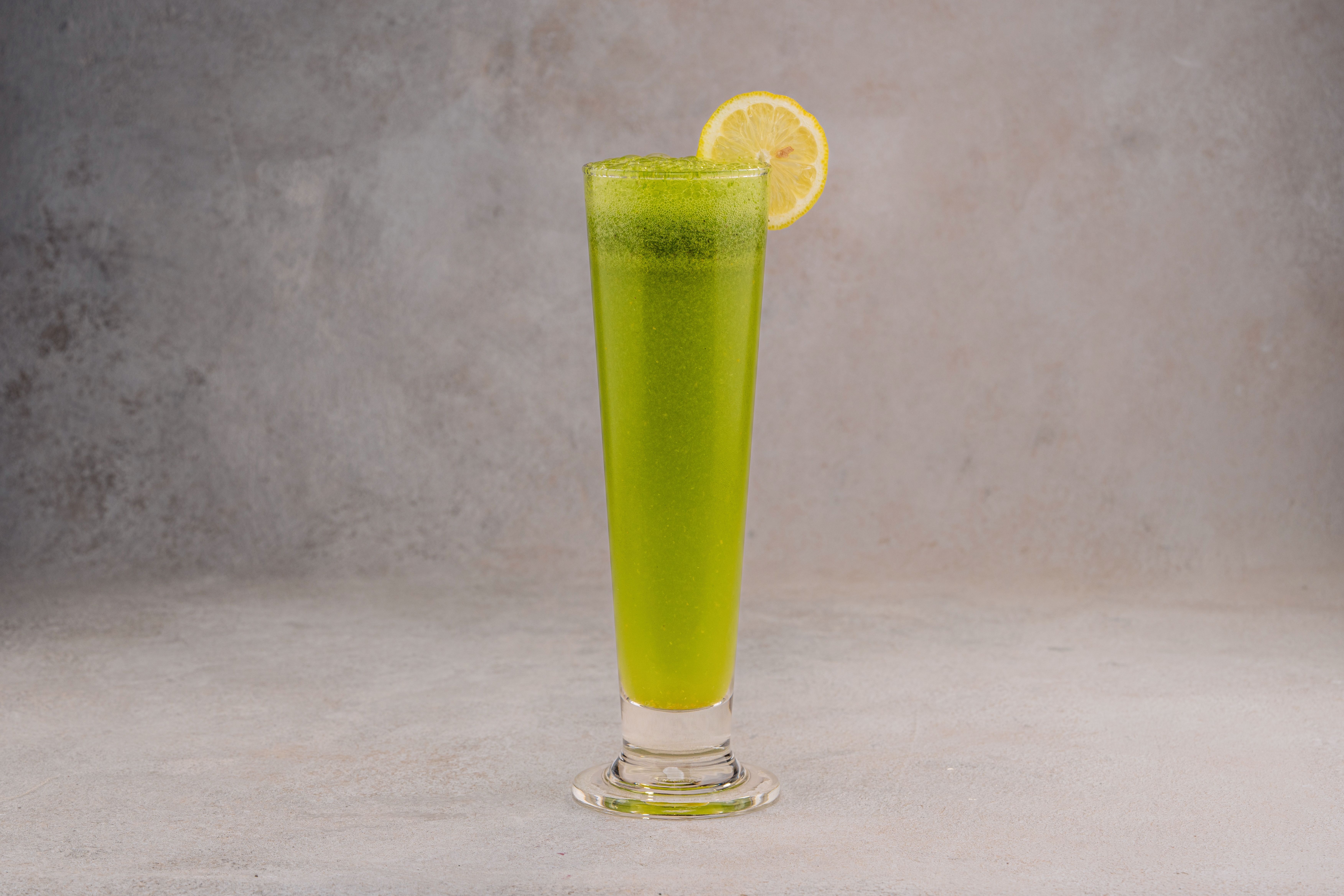 Free Vibrant green drink in a tall glass garnished with a lemon slice against a gray background. Stock Photo