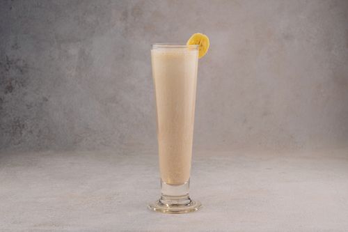 Free Tall glass of banana smoothie with a banana slice garnish against a neutral textured background. Stock Photo