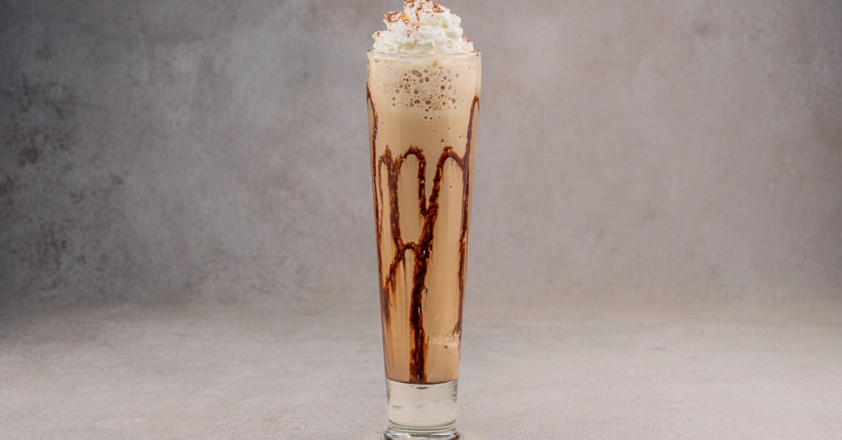 Tall glass of chocolate milkshake topped with whipped cream on a gray background.