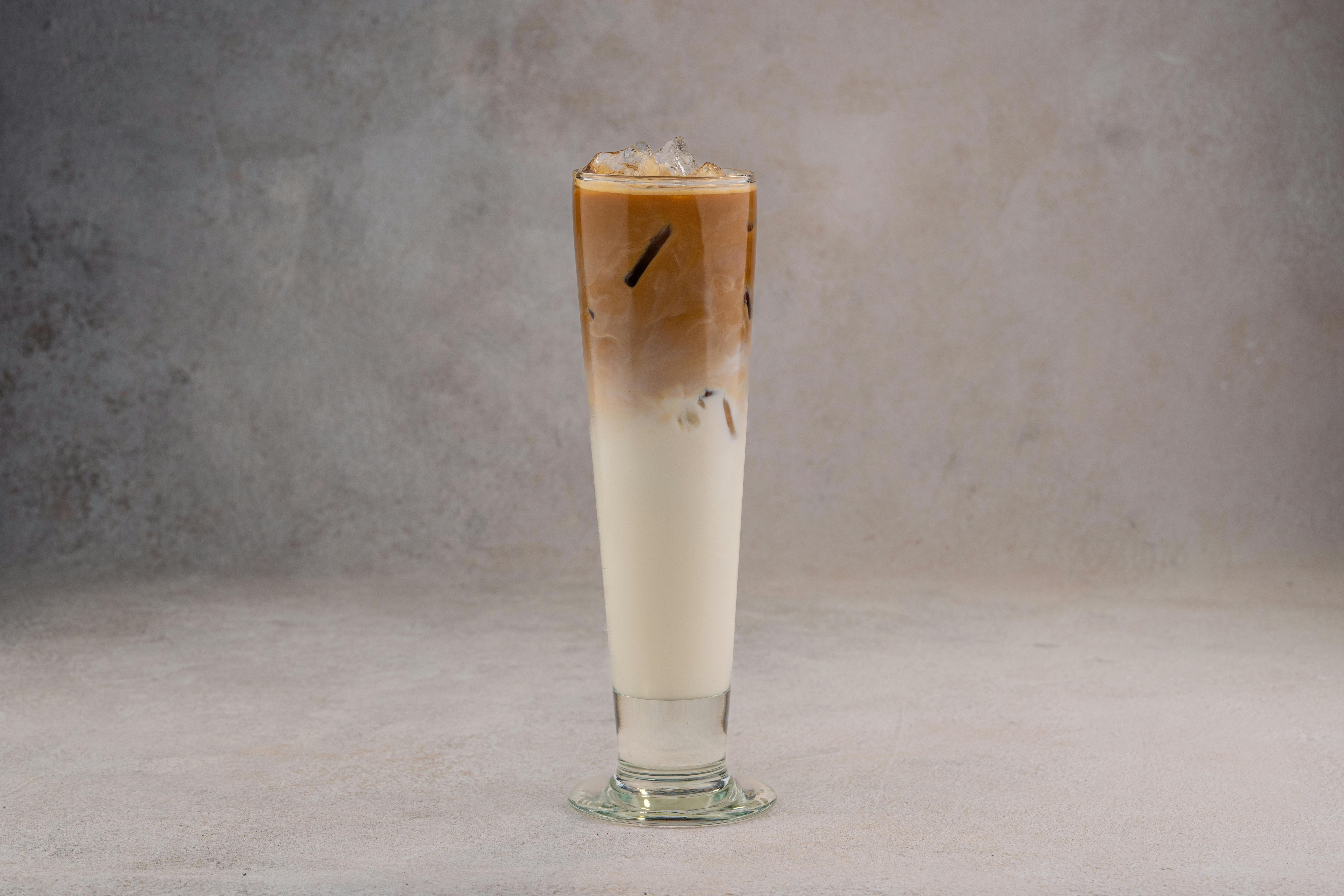 A refreshing iced coffee latte in a tall glass on a neutral gray background.