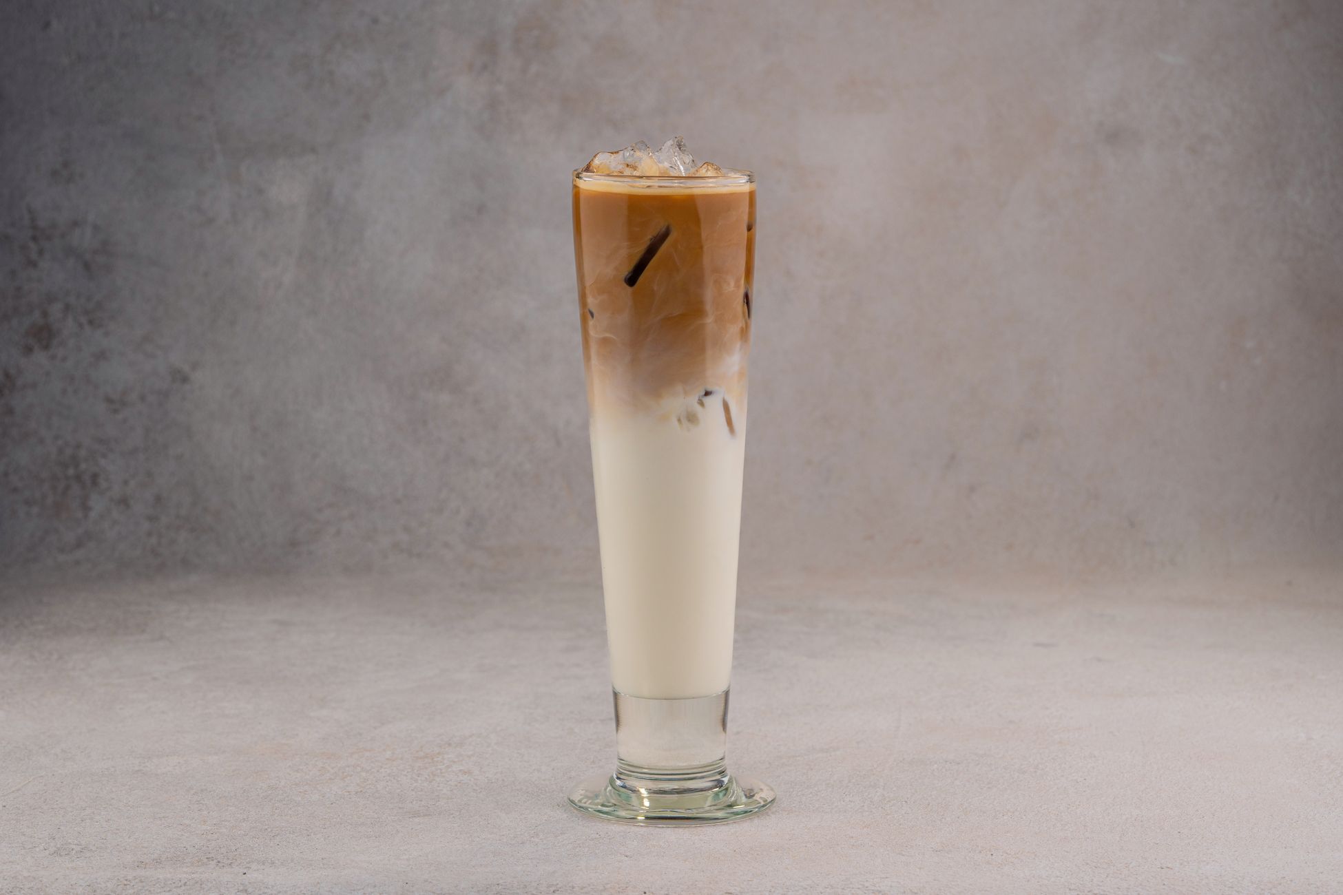 A refreshing iced coffee latte in a tall glass on a neutral gray background.