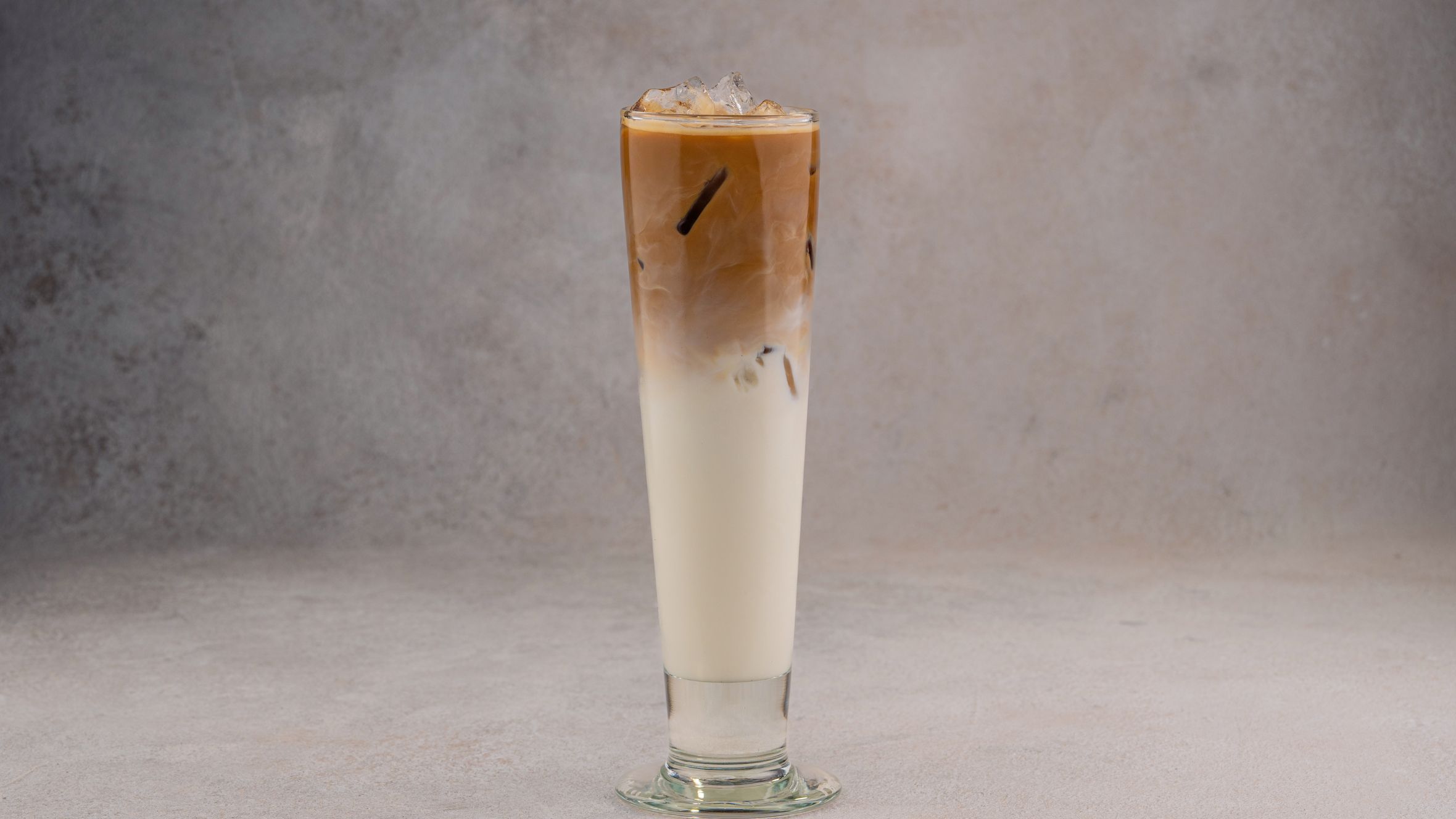 A refreshing iced coffee latte in a tall glass on a neutral gray background.