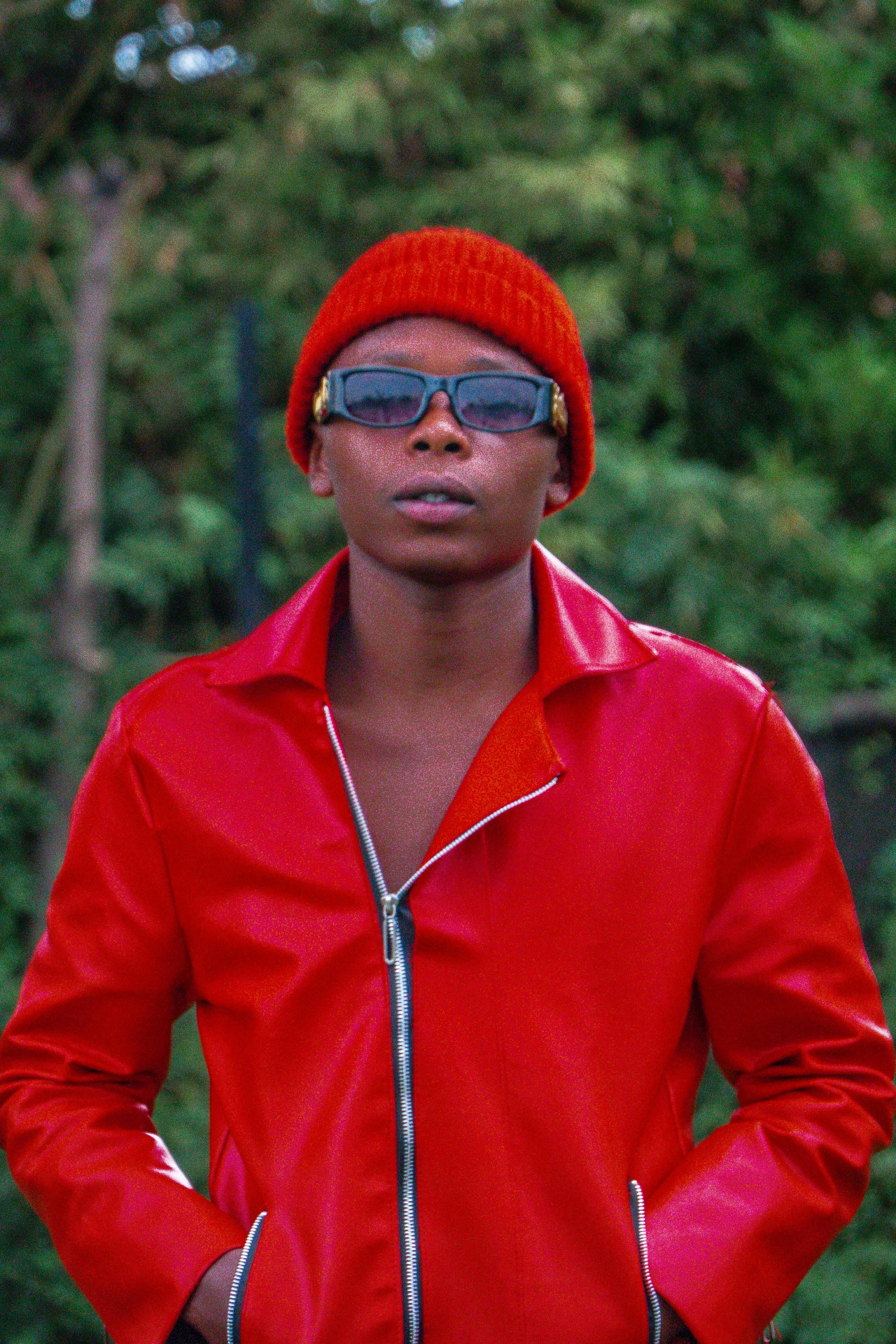 Young man in stylish red jacket and beanie standing outdoors.