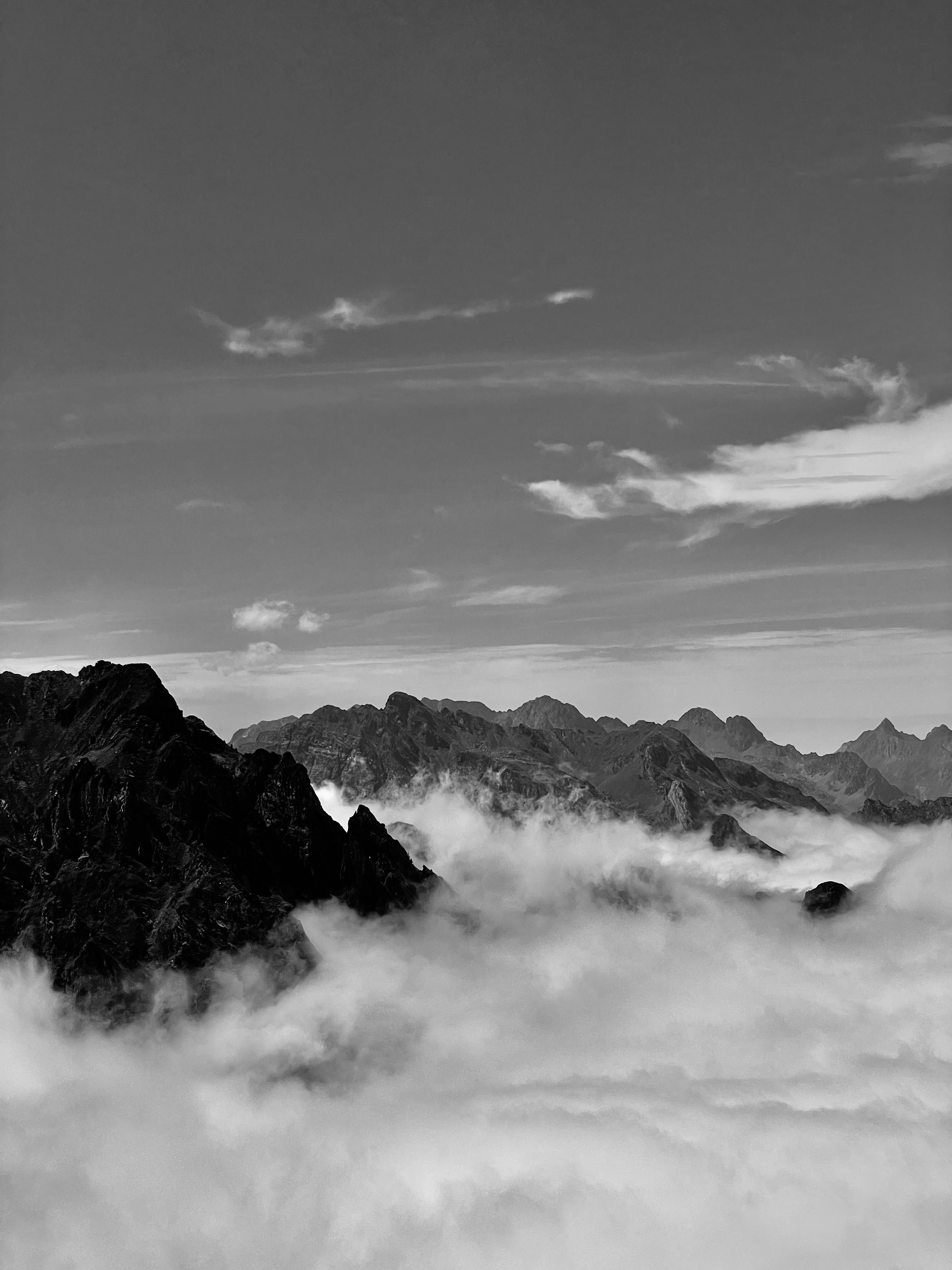 Majestic mountain peaks emerging through clouds in black and white.