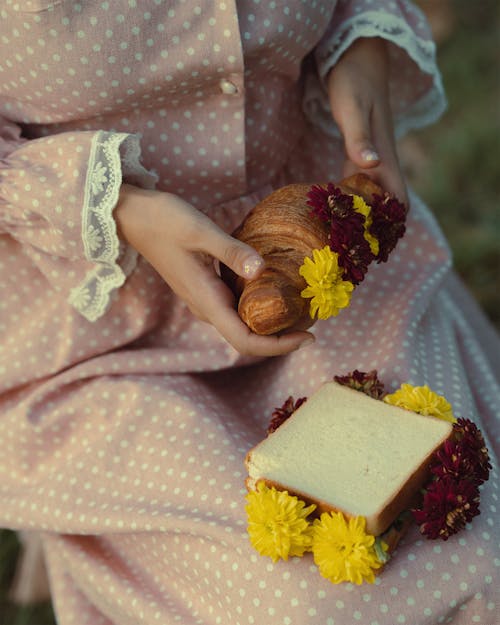 Woman Hands Holding Croissant over Bread and Flowers