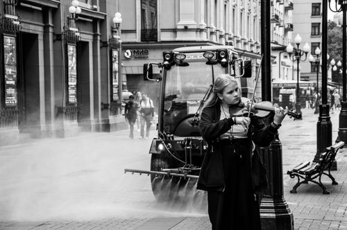 Free Black and white image of a street musician playing violin in a bustling urban alley. Stock Photo