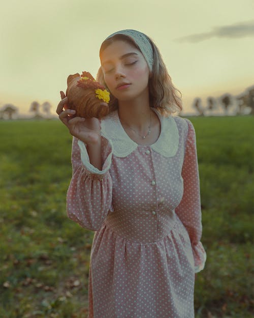 Woman Holding a Croissant on a Field 