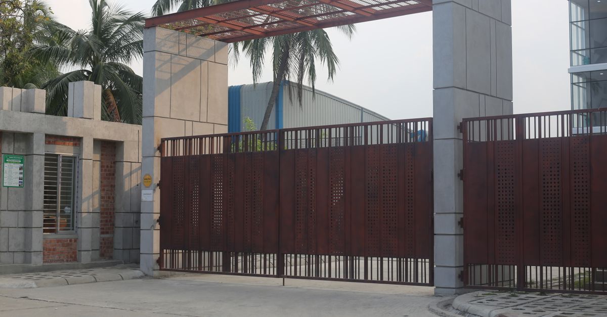 A large automated iron gate as the entrance to a modern urban building, surrounded by palm trees.