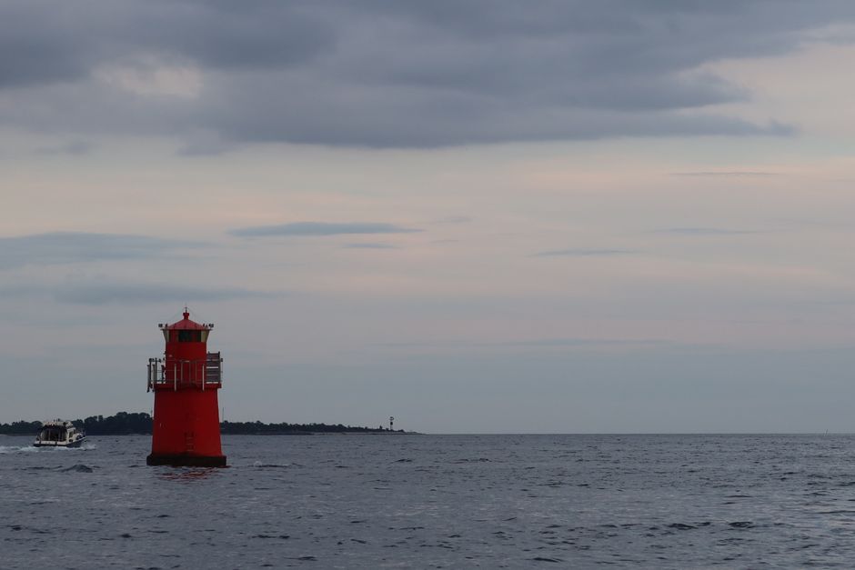 A vibrant red lighthouse stands against a cloudy sky in Fårösund, Sweden, with a boat nearby.