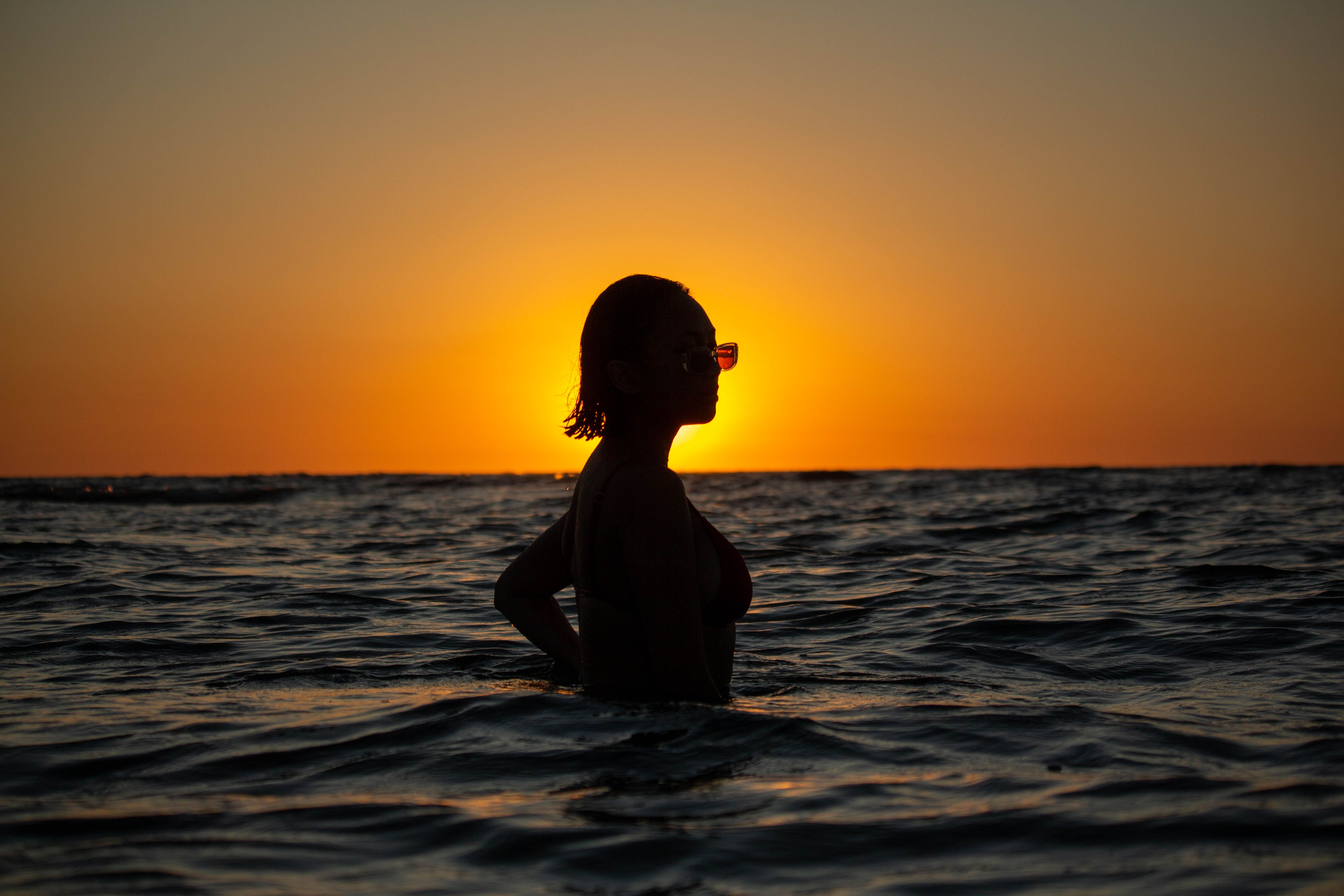 Silhouette of a Woman in a Sea During Sunset · Free Stock Photo