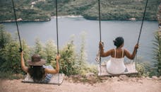 阳光明媚的日子里，两个女人坐在秋千上，俯瞰着湖面放松