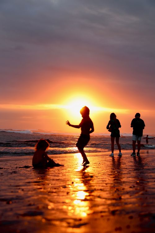 Free Silhouetted people enjoying a sunset on a Bali beach. Stock Photo