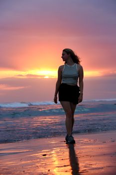 A woman walking on a Bali beach during a vibrant sunset, capturing the essence of a tropical vacation.