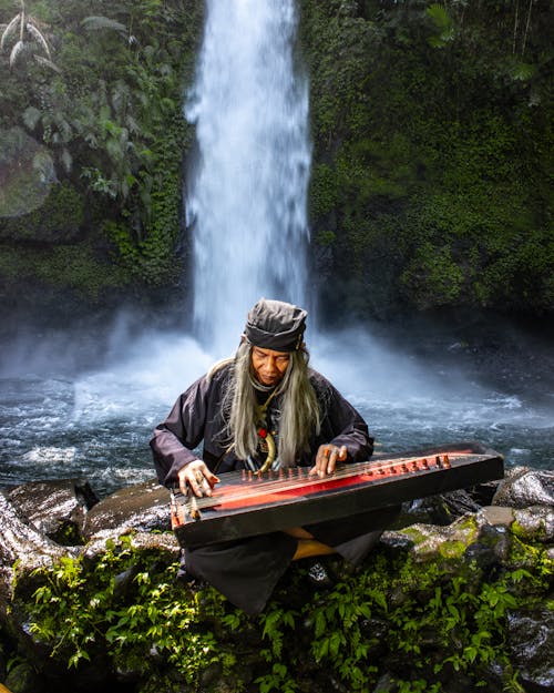 A Woman Playing an Instrument near a Waterfall 