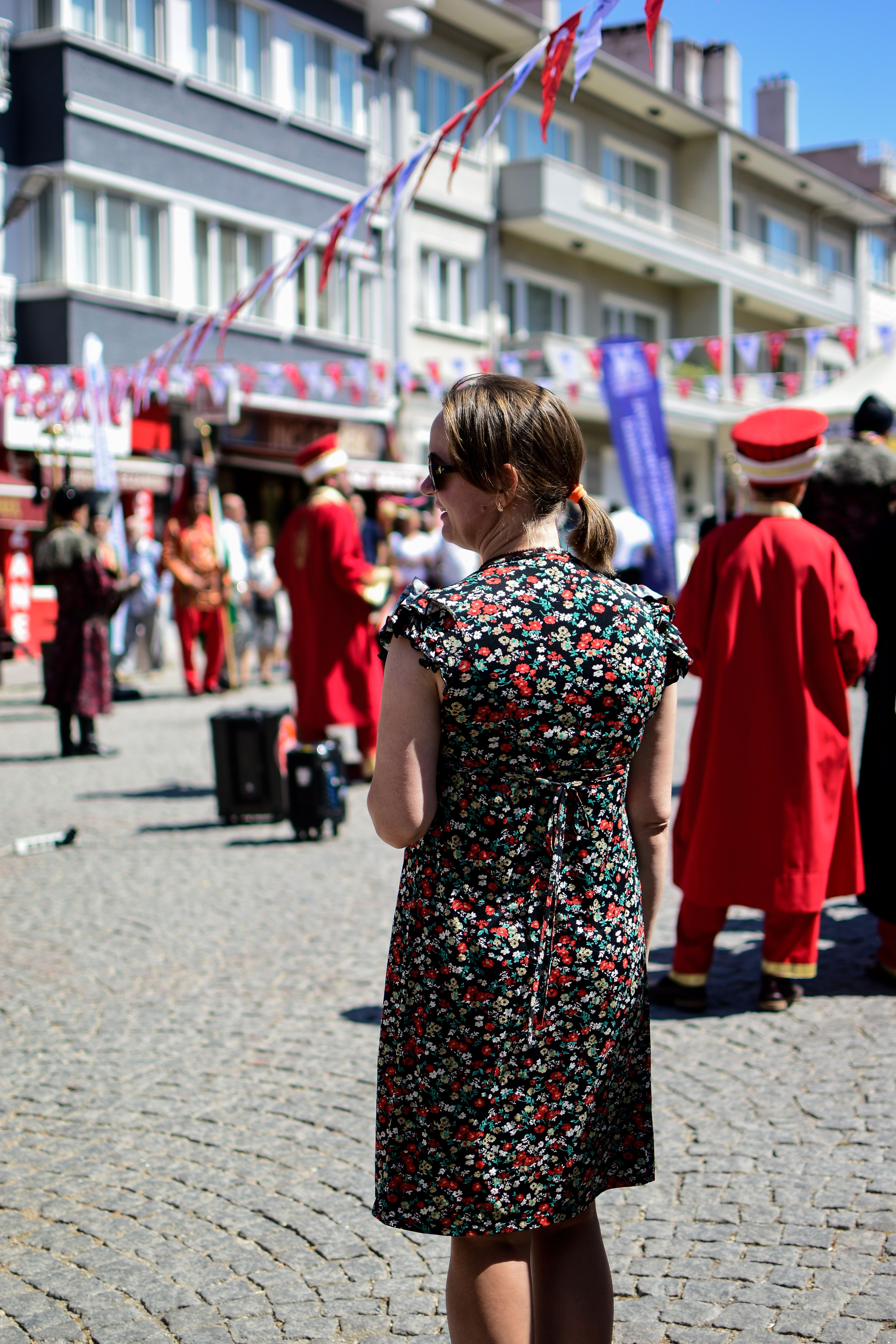 Back view of a woman in a sundress at a lively street festival with performers in traditional attire.
