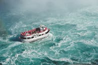 从鸟瞰视角拍摄的尼亚加拉大瀑布旅游船在汹涌水域中穿行，水雾弥漫