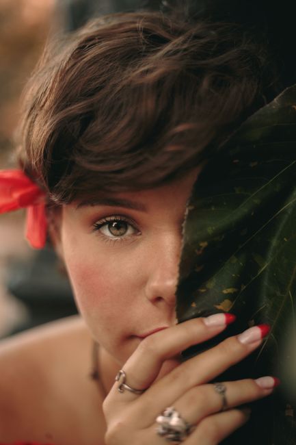 A close-up portrait of a woman partially covered by a leaf, featuring natural beauty and a hint of mystery.