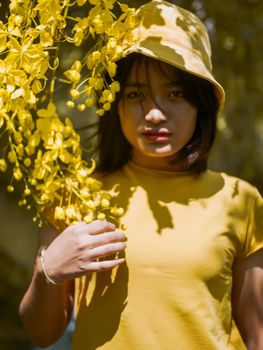 一位身穿黄色服装的亚洲女子在阳光下与鲜艳的黄花合影