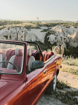 A vintage car parked with a view of hot air balloons in Cappadocia's unique landscape.