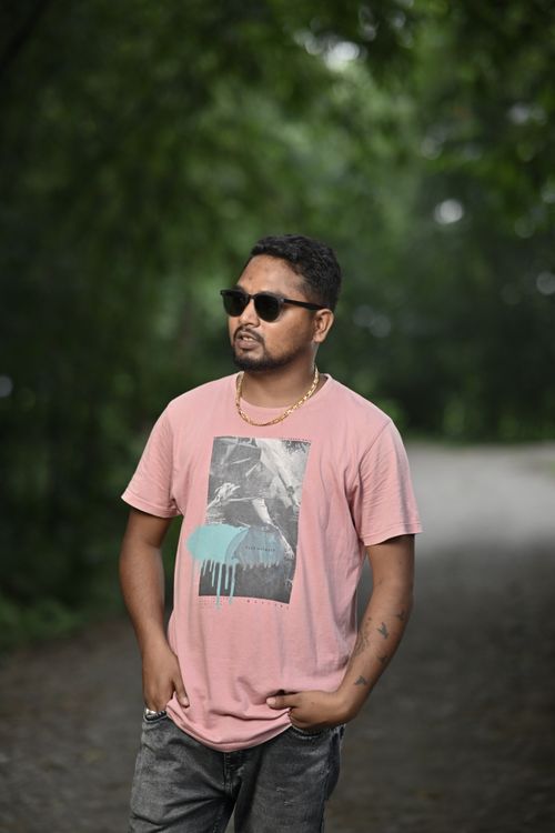 Free Man in sunglasses and pink t-shirt walking on a tree-lined pathway, exuding a casual vibe. Stock Photo