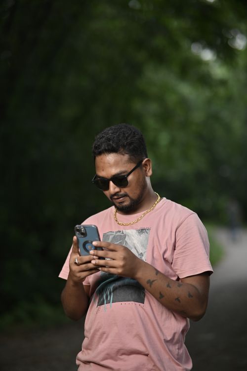 Free Casual man with tattoos uses smartphone outdoors in a pink T-shirt and sunglasses. Stock Photo