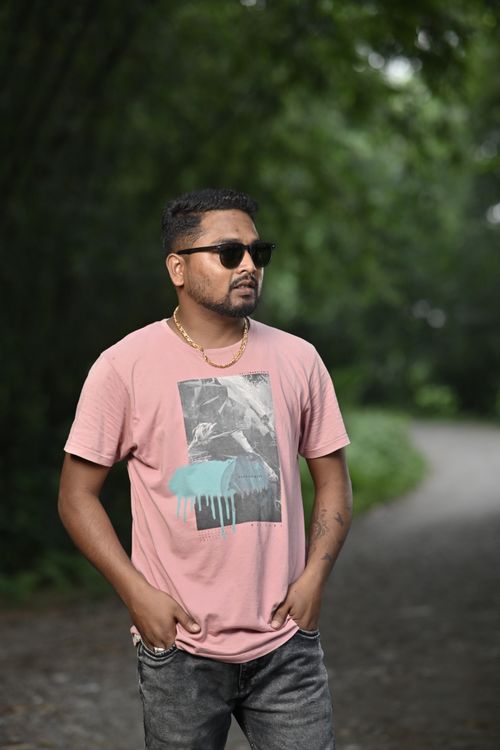Free Man in casual attire with sunglasses stands confidently in a forest trail. Stock Photo